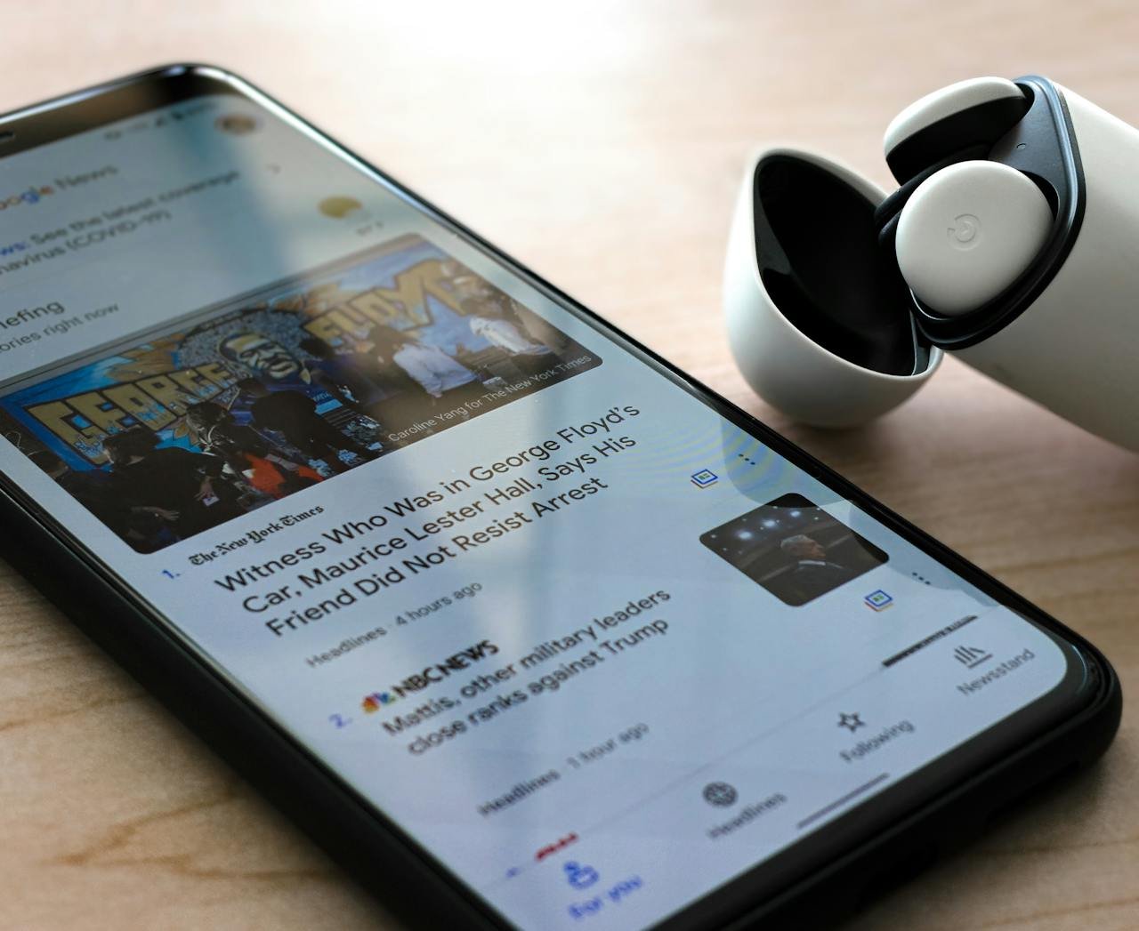 Close-up of a smartphone displaying news with wireless earphones on a table.