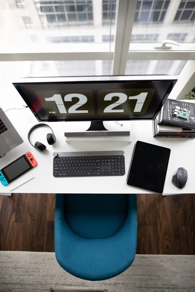 A top view of a modern desk setup featuring a computer monitor, keyboard, tablet, books, and gadgets.