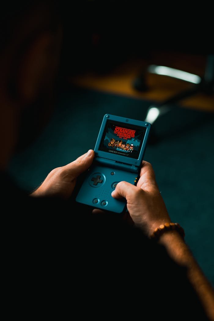 Close-up of individual holding a retro handheld gaming device, playing a classic video game indoors.